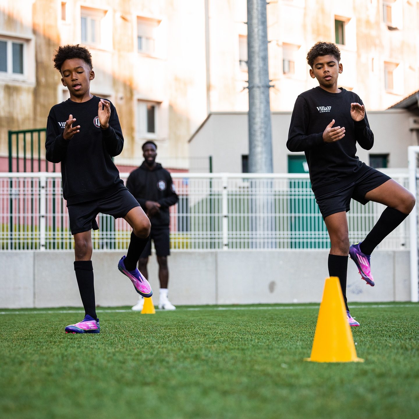 Deux jeunes joueurs à l'entraînement, cônes au sol, éducateur en arrière-plan